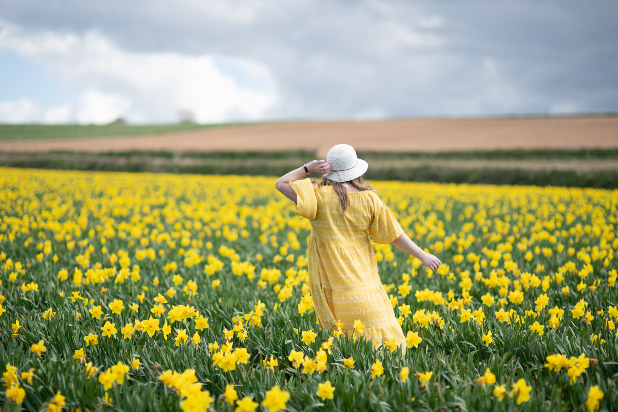 Over 40 fashion blogger in a yellow summer dress in a field of daffodils
